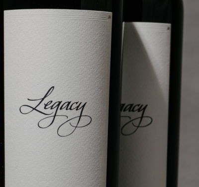 Two bottles of red wine lined up against a gray background