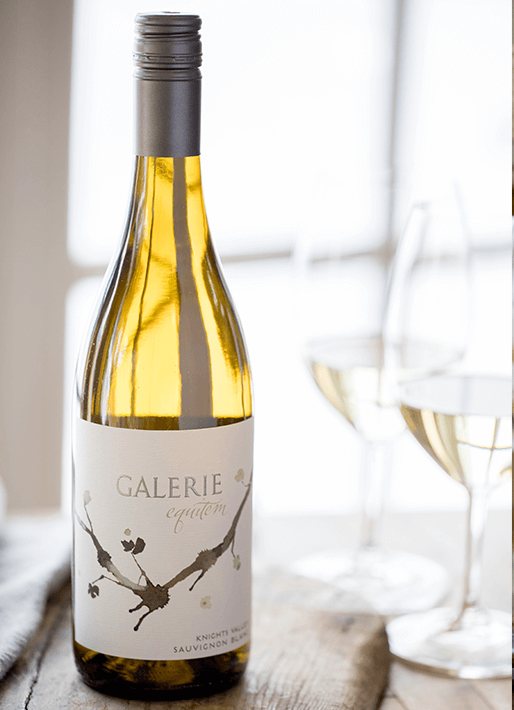 2018 Galerie Equitem wine bottle with a wine glass to the right against a blurred window letting light in