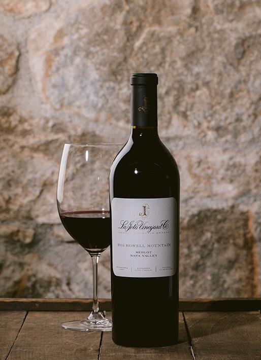 Wine bottle against a stonebackdrop with a wine glass off to the side with red wine