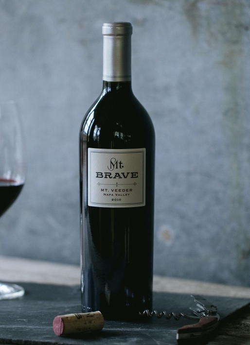 Bottle of wine with a slate gray background and two wine glasses on the left