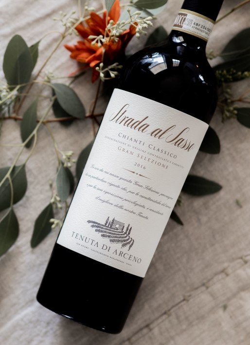 Single bottle of red wine laid down on a white table clothes with fall leaves behind the wine.